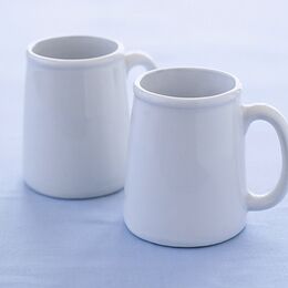 Due mug in ceramica bianca lucida senza decori, affiancati e ripresi di tre quarti, su fondo azzurro chiaro.