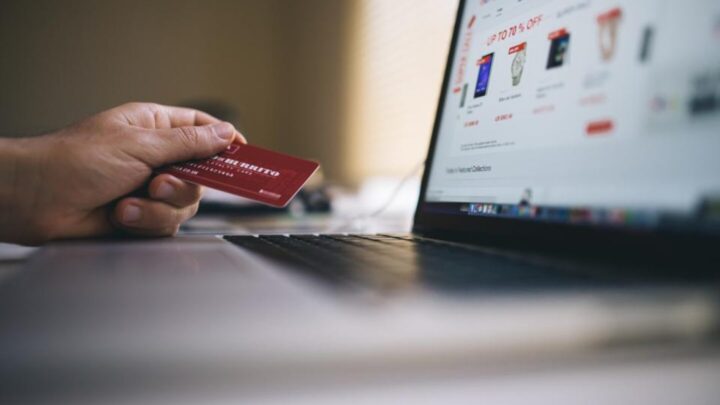 Mano che tiene una carta di credito davanti a un computer portatile con un e-commerce aperto
